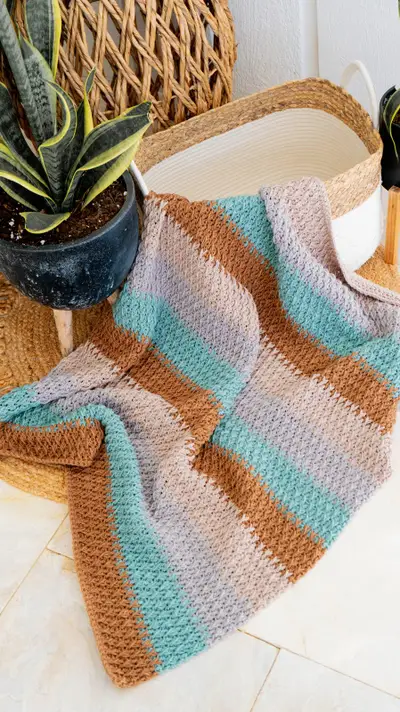 Alpine Stitch Blanket folded in a woven basket with a potted plant