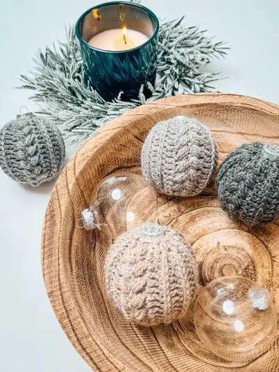 Bowl of textured Autumn Wheat Bauble Ornaments in gray and cream beside a lit candle