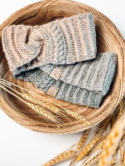 Autumn Wheat Ear Warmers in oatmeal and sage with a twisted front, in a wooden bowl