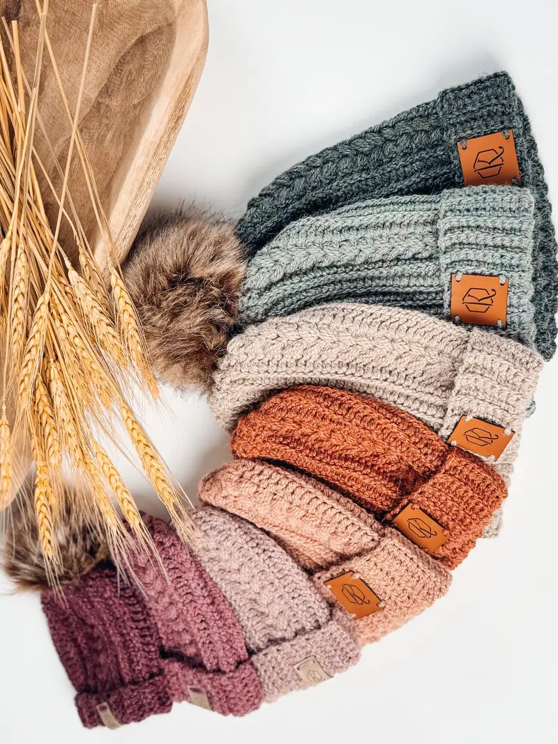 Row of Autumn Wheat Flat Crochet Hats in sage, rust, peach and plum with faux fur pom poms