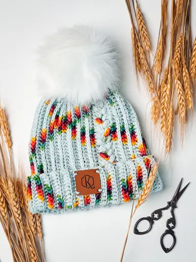 Autumn Wheat Flat Crochet Hat in light blue with rainbow speckles and a white pom pom