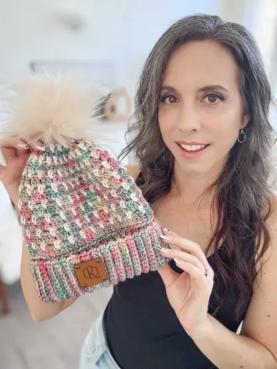 Smiling woman holding a pink speckled Block Stitch Beanie with a leather tag