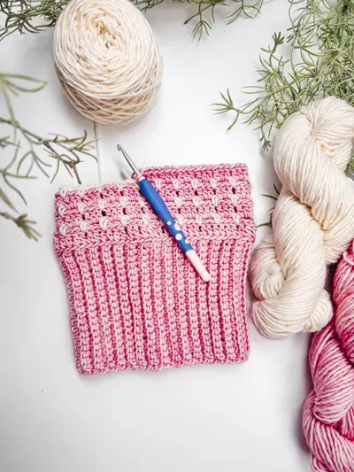 Block Stitch Beanie in progress in pink with a crochet hook and skeins of yarn