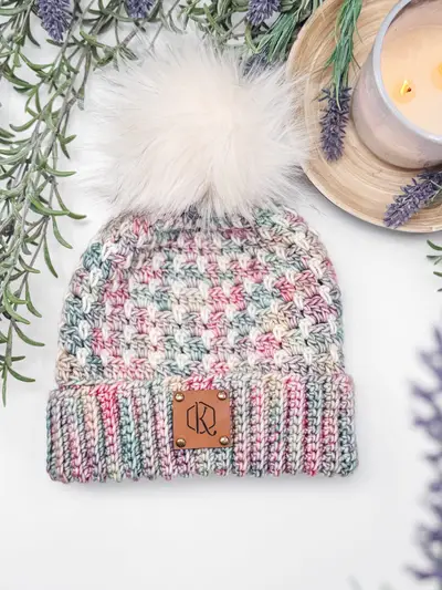 Speckled pink Block Stitch Beanie with a cream pom pom and leather patch