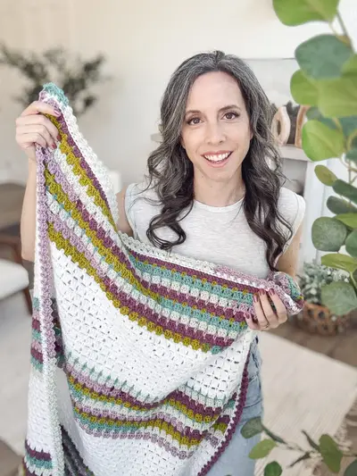 Smiling woman showing the Block Stitch Crochet Blanket with its colorful striped border