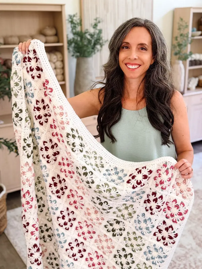 Woman holding up the Blossom Granny Square Blanket in cream with red, pink, green and blue flowers