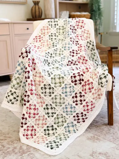 Blossom Granny Square Blanket draped over a chair, cream squares with colorful flowers