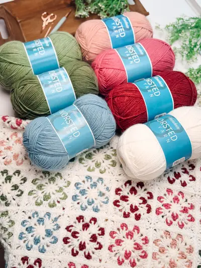Skeins of green, pink, red, blue and cream yarn on top of the Blossom Granny Square Blanket