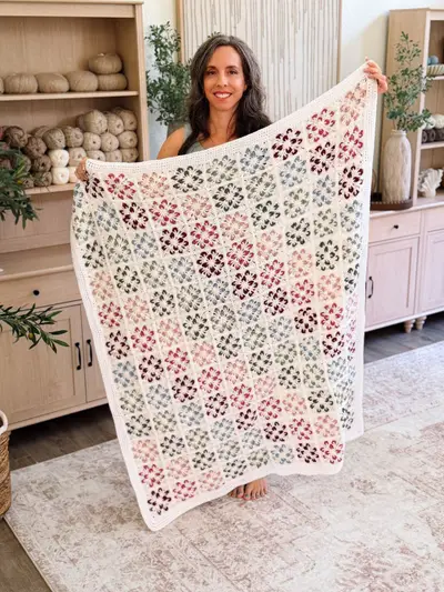 Woman holding the finished Blossom Granny Square Blanket in front of a bookcase