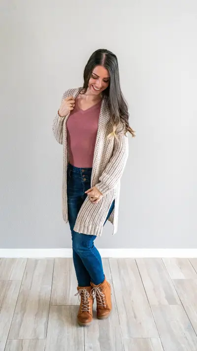 Woman in the long cream Campside Crochet Cardigan over a pink top with jeans and boots