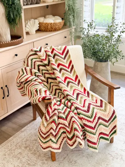Chevron Petal Loop Blanket in red, green and cream holiday stripes draped on an armchair