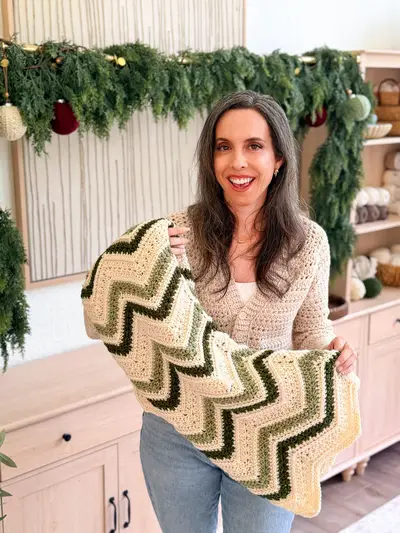Woman holding the cream and green Chevron Petal Loop Blanket in a holiday room