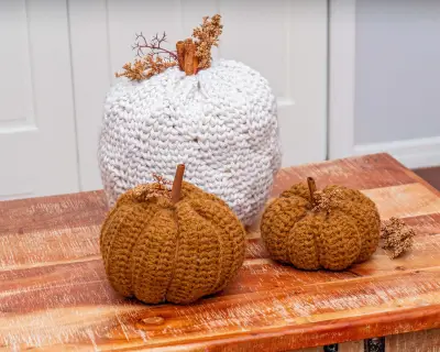 Cream Cinderella's Crochet Pumpkin with two mustard pumpkins on a rustic wooden bench