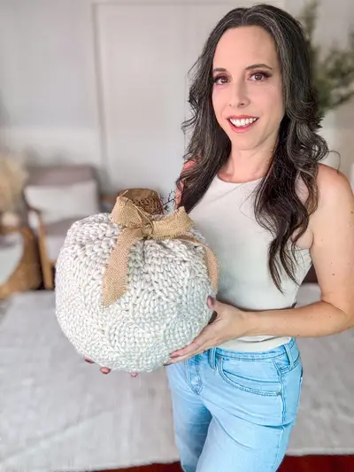 Smiling woman holding a cream Cinderella's Crochet Pumpkin with a burlap bow