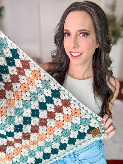 Close up of the Colorful Hues Crochet Blanket held up by a smiling woman