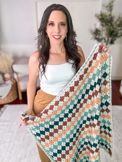 Woman holding the Colorful Hues Crochet Blanket with its teal, peach and rust rows