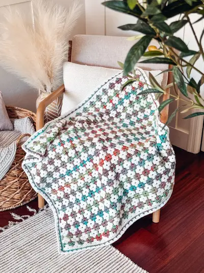 Colorful Hues Crochet Blanket in muted multicolor draped over a chair