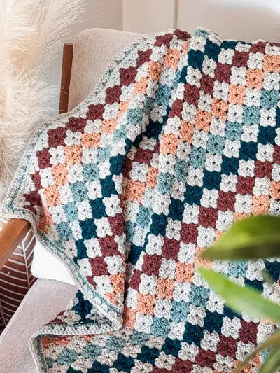 Colorful Hues Crochet Blanket in rust, peach, navy and teal over a chair