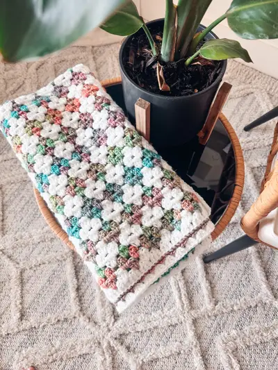 Speckled multicolor Colorful Hues Crochet Blanket folded under a potted plant