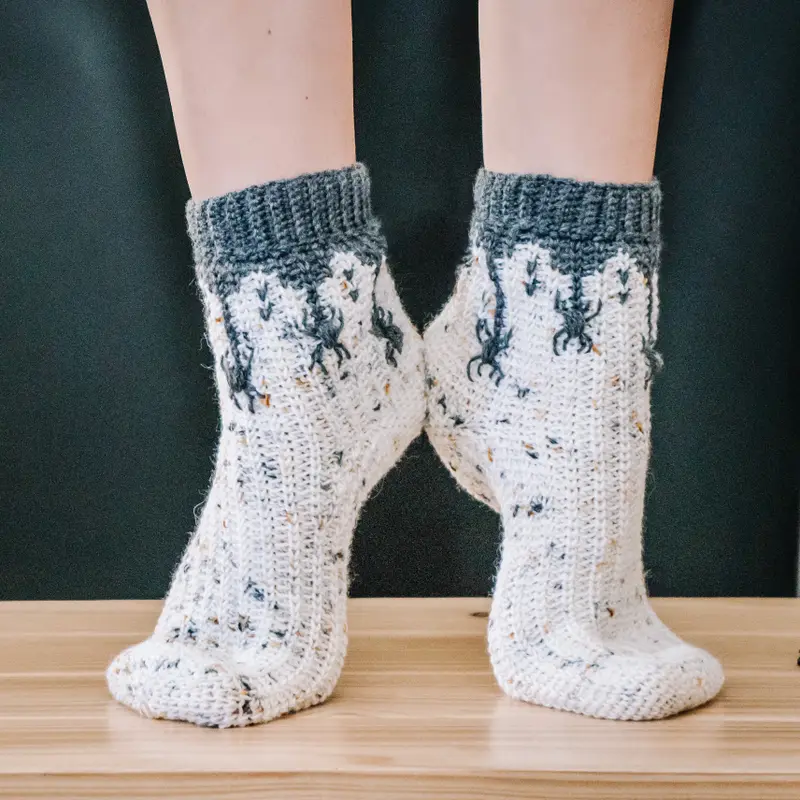 Feet wearing Creepy Crawly Spider Crochet Socks in speckled cream with charcoal spiders and cuffs