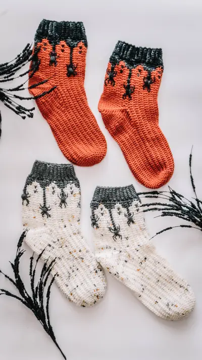 Two pairs of Creepy Crawly Spider Crochet Socks laid flat, one orange and one cream