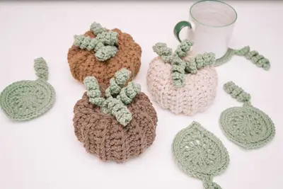 Brown and cream crochet pumpkins with sage leaf coasters and a candle