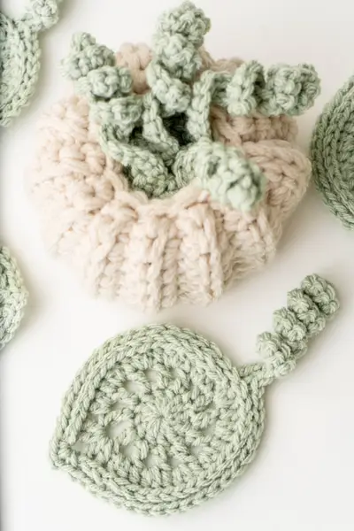 Close up of a cream crochet pumpkin with curly sage tendrils and a leaf coaster
