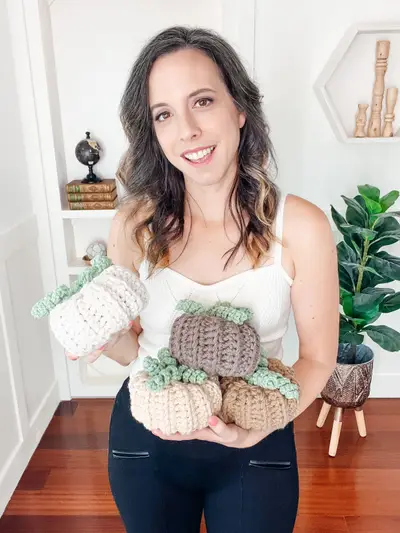 Woman holding an armful of crochet pumpkins in cream, brown and sage