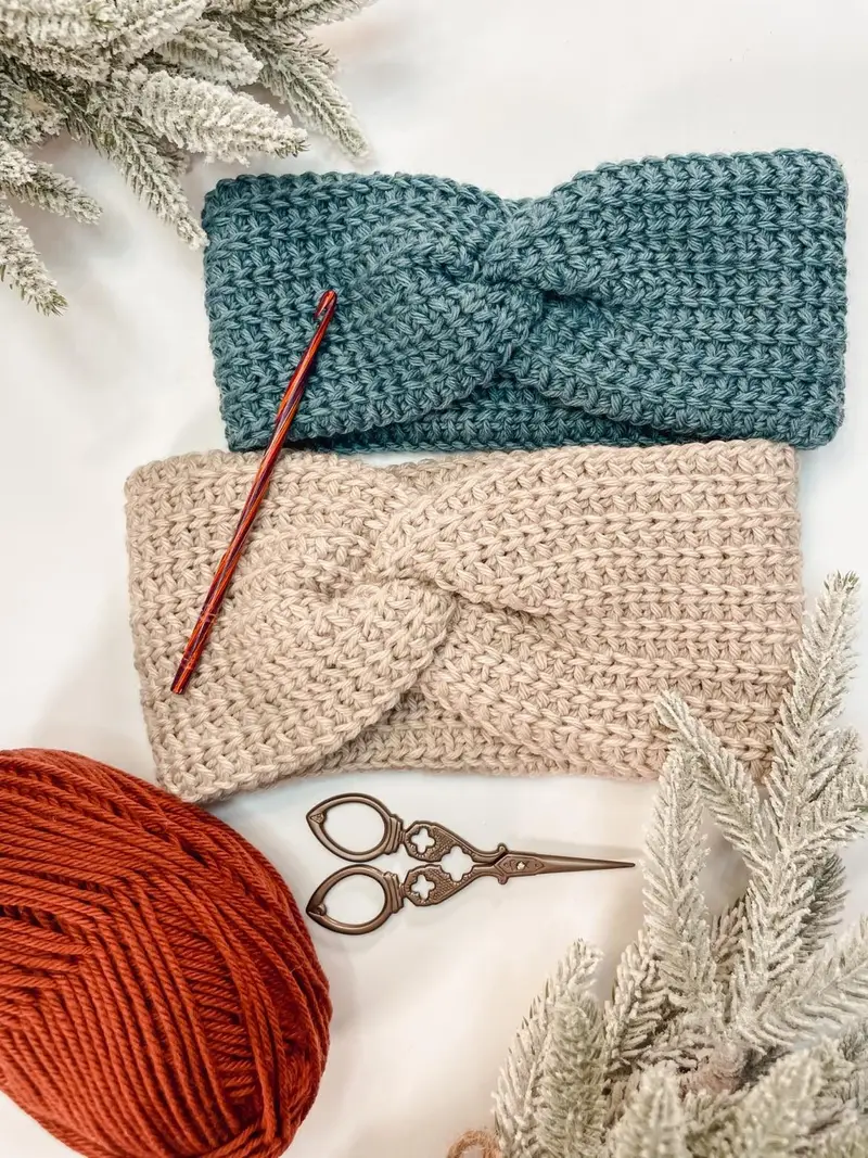 Easy Crochet Ear Warmers in teal and oatmeal with a twist front, beside a crochet hook and yarn