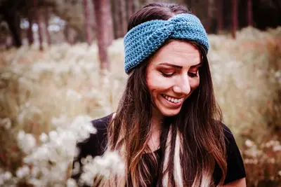 Smiling woman wearing a teal Easy Crochet Ear Warmer outdoors