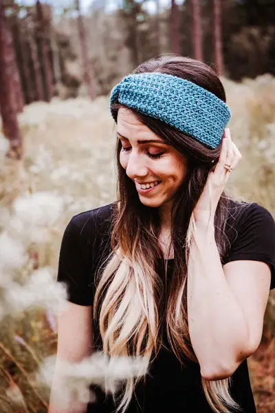 Woman in a teal Easy Crochet Ear Warmer looking down, golden field behind her