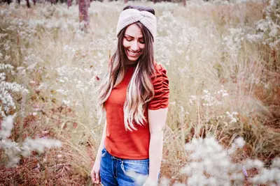 Woman wearing an oatmeal Easy Crochet Ear Warmer and an orange top in a field