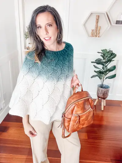 Woman wearing the teal ombre Enchanted Crochet Poncho with a leather backpack