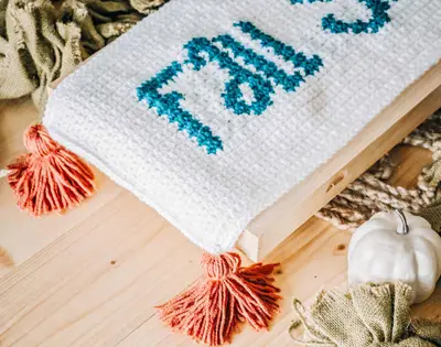 Close up of the table runner corner with teal lettering and an orange tassel