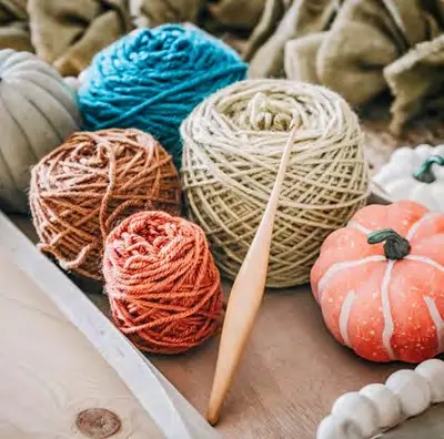 Balls of teal, cream, rust and orange yarn with a wooden hook and pumpkin