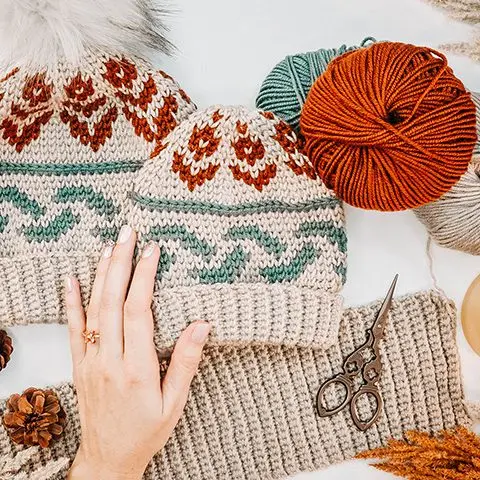 Forest Brooks Crochet Beanies in oatmeal with rust and teal colorwork beside skeins of yarn
