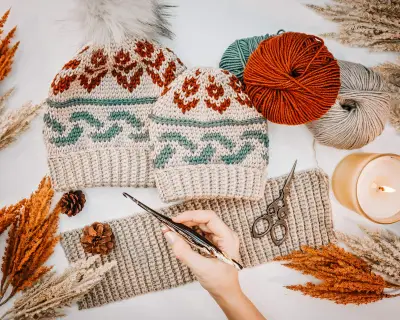 Hands crocheting a Forest Brooks Crochet Beanie with rust and teal yarn and autumn decor