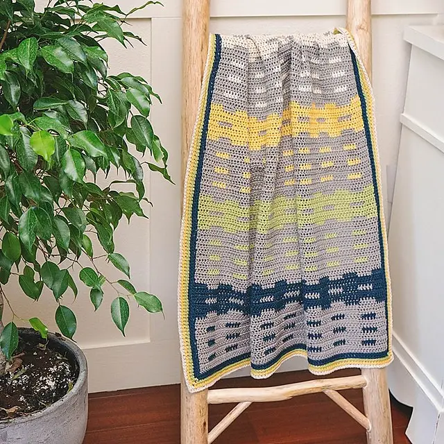 Garden Fences Crochet Blanket in gray, navy, yellow and green stripes on a ladder
