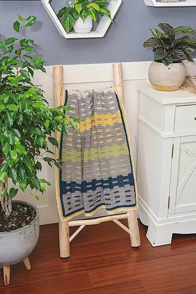 Garden Fences Crochet Blanket hanging on a ladder beside a potted plant