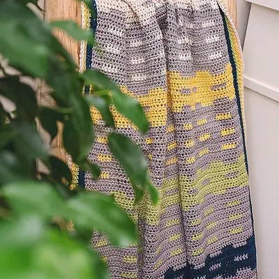 Garden Fences Crochet Blanket draped on a ladder behind greenery