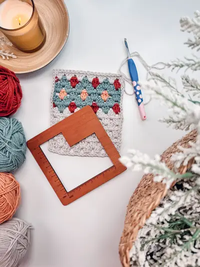 Gemstone Hues diamond motif with skeins of yarn, a hook and a wooden blocking frame
