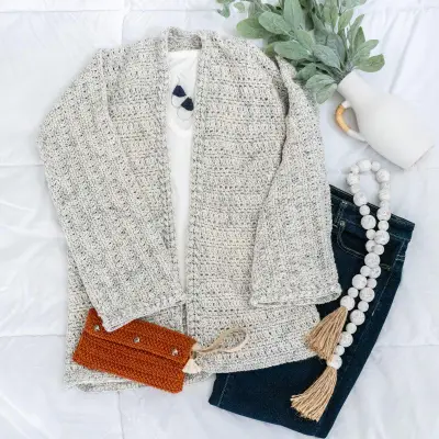 Flat lay of the oatmeal Get Comfy Crochet Cardigan with jeans and a bead garland