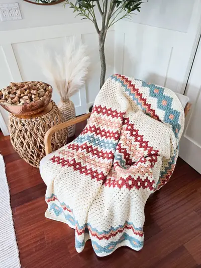 Gemstone Hues Crochet Blanket in cream with rust, blush and blue zigzag stripes on an armchair