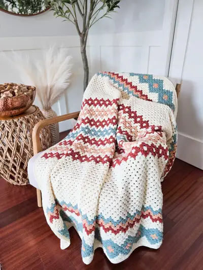 Cream Gemstone Hues Crochet Blanket with rust and blue borders on a chair