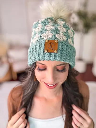 Woman wearing a teal and cream Harvest Hues Crochet Beanie with a faux fur pom pom