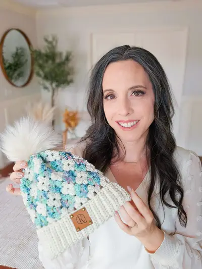 Woman holding a teal and cream Harvest Hues Crochet Beanie with a faux fur pom pom