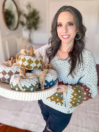 Woman holding a tray of Harvest Hues Crochet Pumpkins in teal, rust and gold