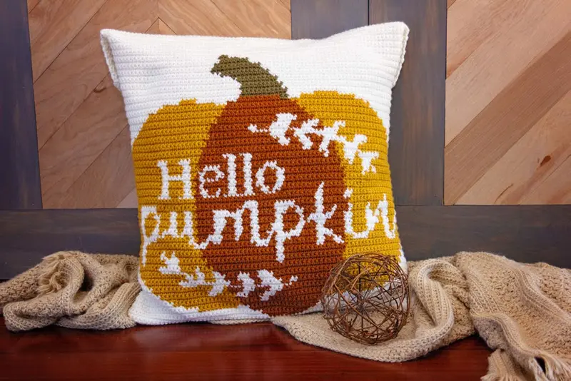 Hello Pumpkin Crochet Pillow with a mustard and rust pumpkin on a wooden bench