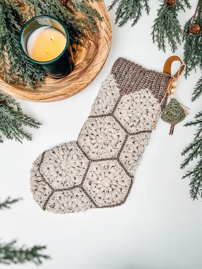 Oatmeal and sage Hexagon Granny Stocking beside a candle and pine