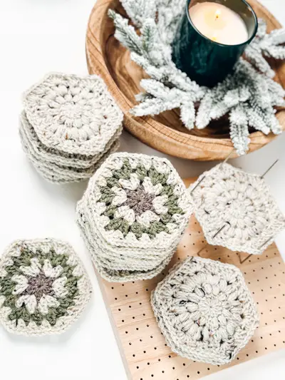 Stack of oatmeal and sage hexagon granny squares on a pegboard with a candle